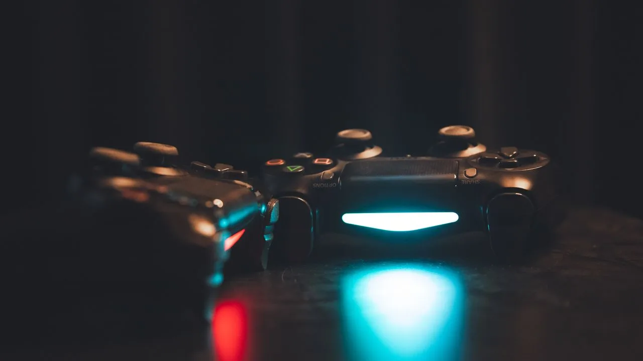 Zwei Gaming-Controller im Dunkeln mit blauem und rotem Leuchten als Sinnbild für die jahrelange Vorfreude auf ein Spiel