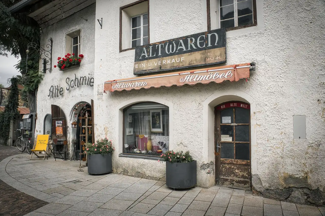 Altes Geschäftslokal mit handgemalter Aufschrift Altwaren und roter Markise, davor Blumentröge und ein Fahrrad