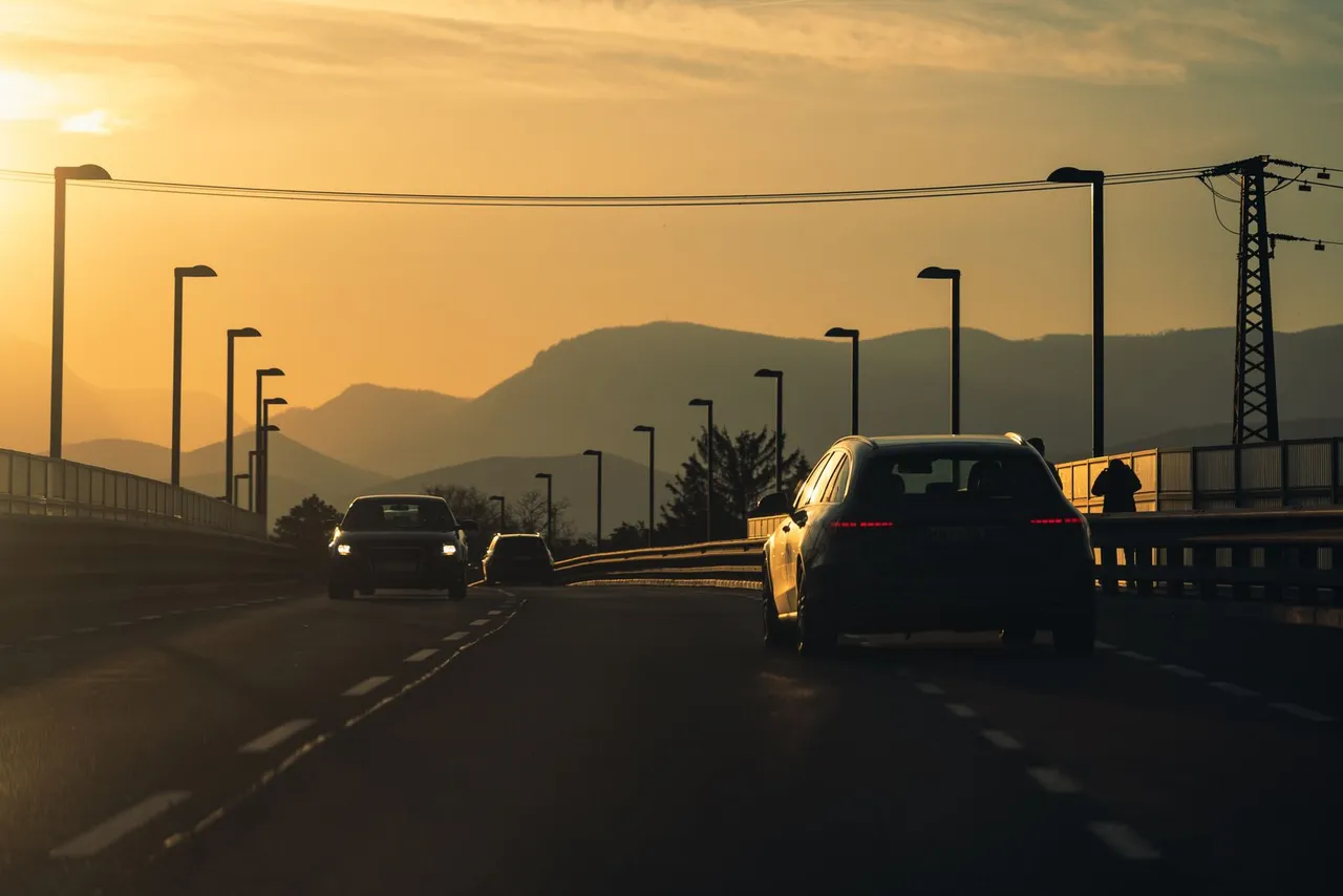 Autos auf einer Schnellstraße im Gegenlicht der untergehenden Sonne, im Hintergrund die Hügelkette des Wiener Beckens