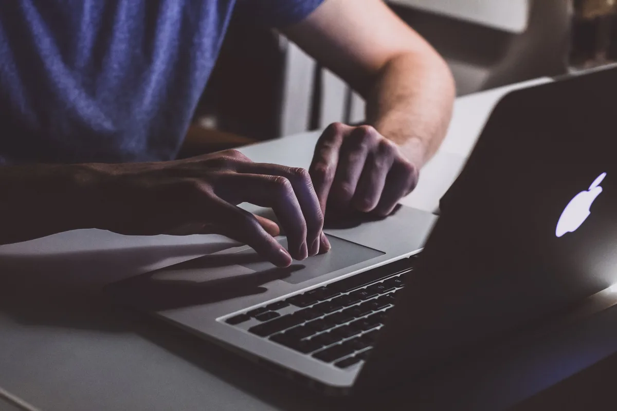 Hände tippen in einem abgedunkelten Büro auf einem Laptop: Sinnbild für die schriftliche Anfrage beim Hoster, ob die PHP-Sicherheitslücke auf der eigenen Website geschlossen ist
