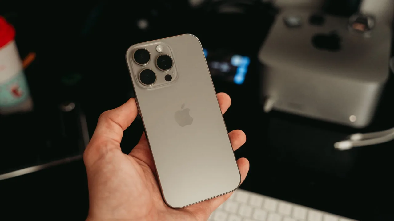 Hand hält ein modernes iPhone vor einem Apple-Arbeitsplatz als Sinnbild für die Tempo- und Datenschutz-Neuerungen in iOS 27