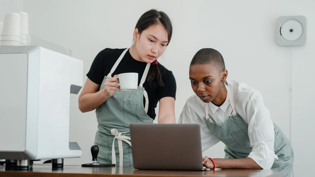 Zwei Betreiberinnen eines kleinen Cafés schauen gemeinsam auf einen Laptop und planen ihre Website