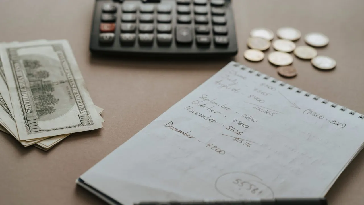 Taschenrechner, Bargeld und ein handschriftliches Budget-Notizbuch auf einem Tisch als Sinnbild für die Kostenplanung einer Website