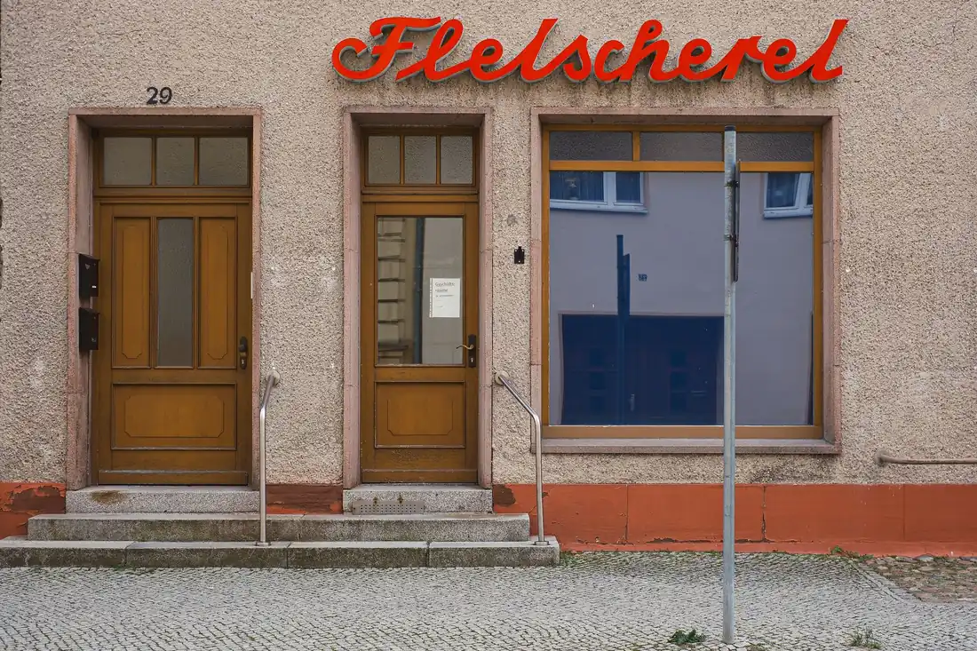 Historische Fassade einer Fleischerei mit alter Leuchtschrift und zwei Holztüren an einer Ortsdurchfahrt