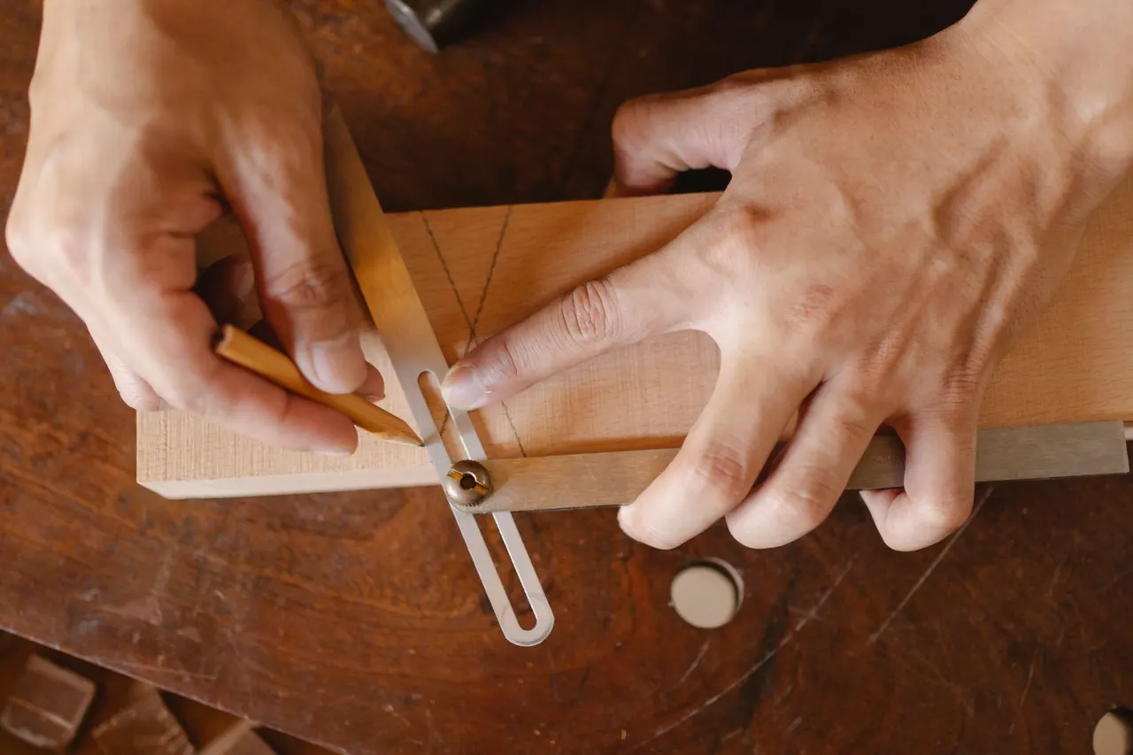 Hände eines Handwerkers messen mit einer Schmiege und einem Bleistift einen Winkel an einem Holzbrett an