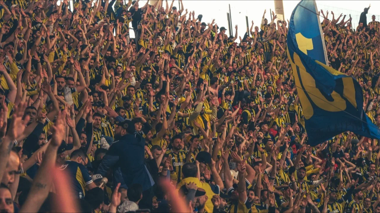 Jubelnde Fußballfans mit erhobenen Armen auf einer vollen Stadiontribüne als Sinnbild für Begeisterung bei der WM