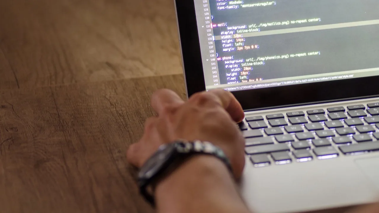 Hand mit Armbanduhr tippt Code auf einem Laptop als Sinnbild für Zeit und Tempo bei der Website-Erstellung