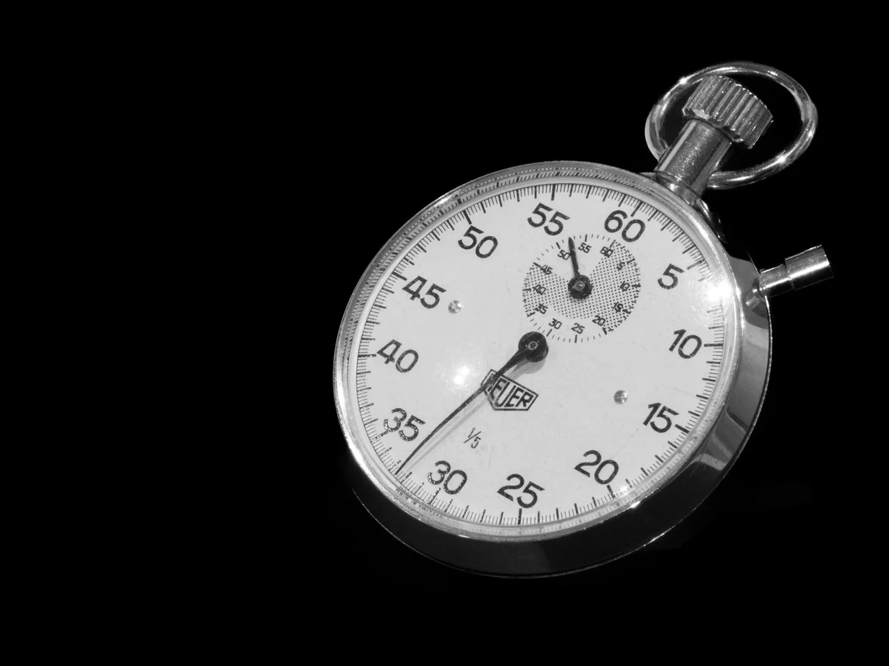 Mechanische Stoppuhr mit weißem Zifferblatt vor schwarzem Hintergrund