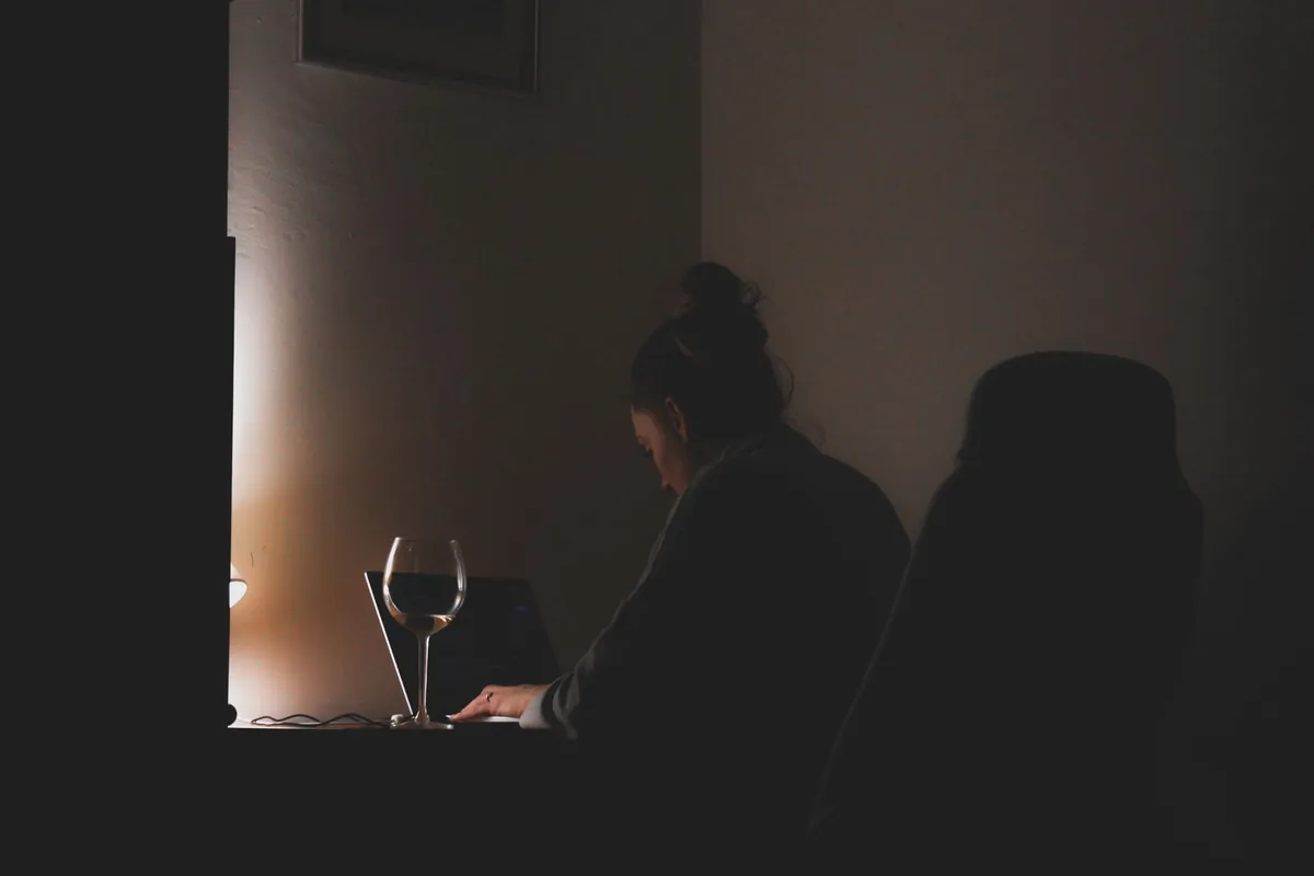 Frau sitzt abends im dunklen Zimmer vor dem aufgeklappten Laptop, neben ihr ein Weinglas: der typische Moment, in dem jemand merkt, dass die eigene WordPress-Seite nicht mehr lädt